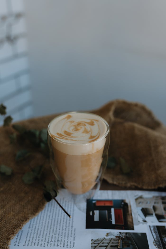 services-03 Elegant coffee drink with swirled foam in glass on rustic burlap with magazine backdrop.